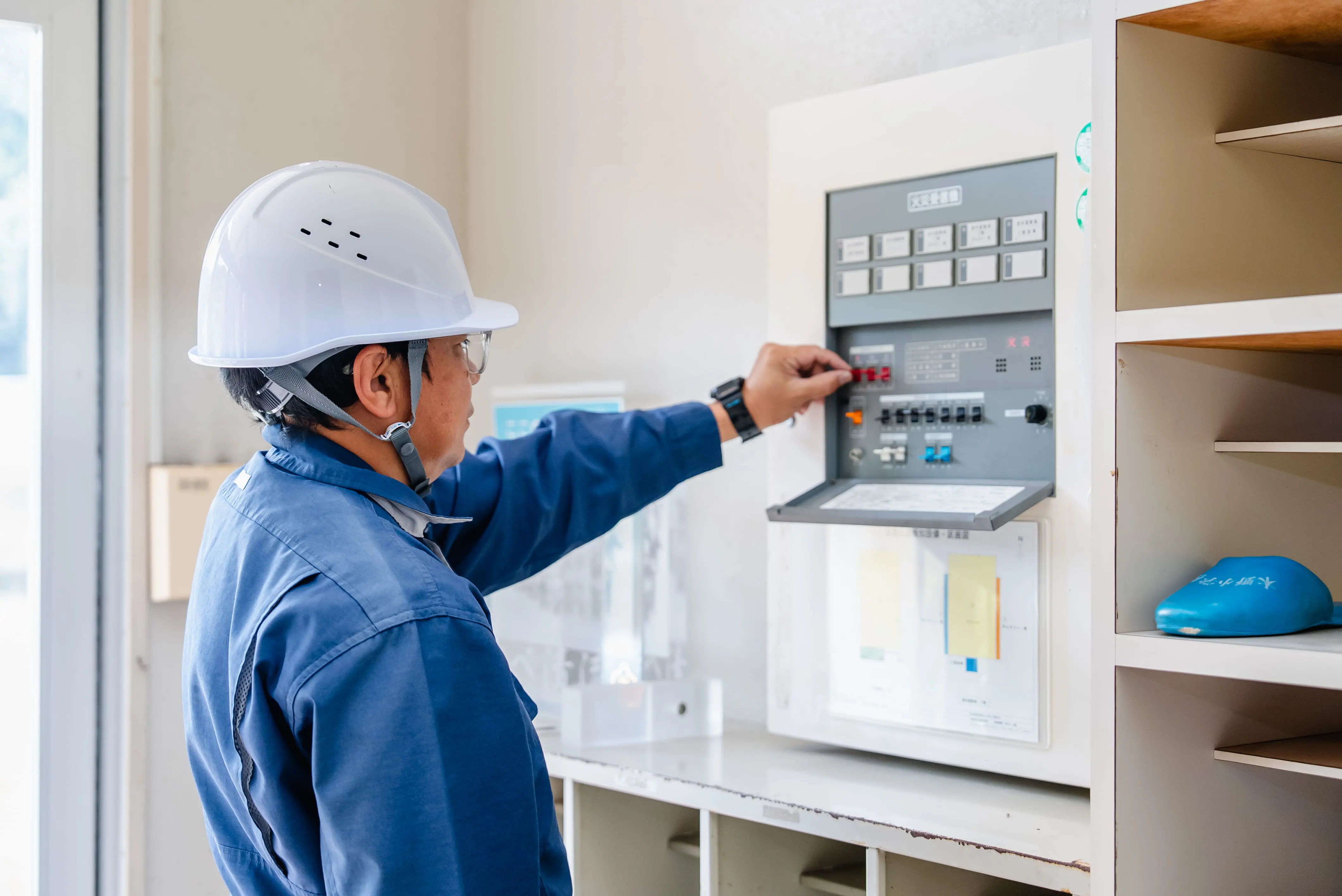 作業員が、室内の分電盤を開けて表示やスイッチを確認し、電気設備を点検している様子