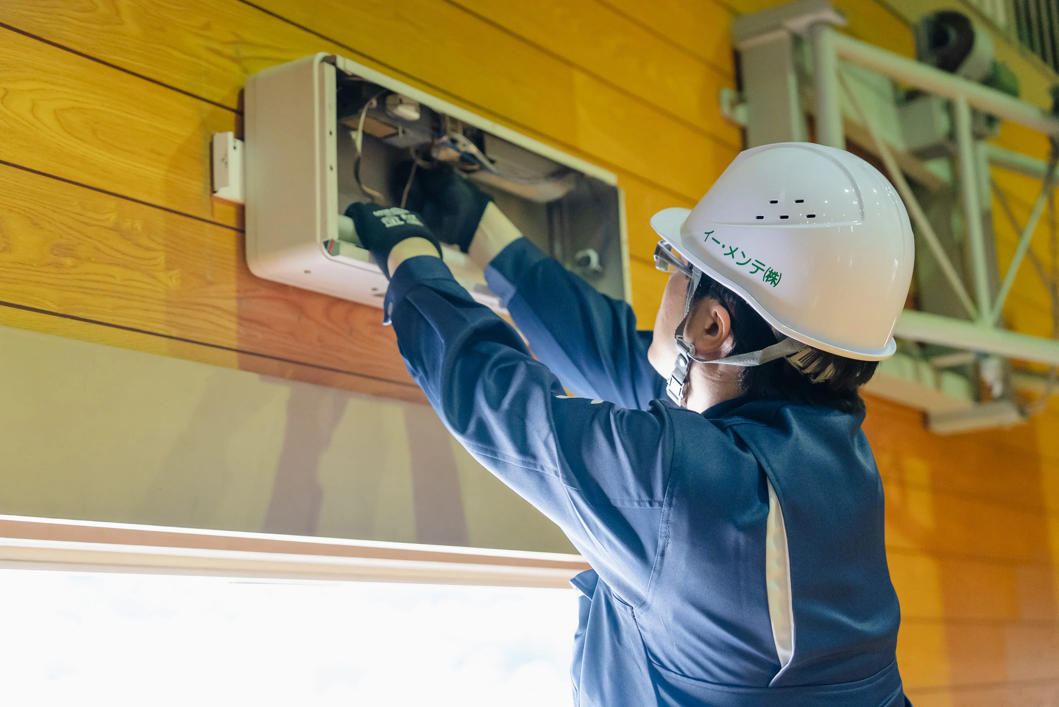 作業員が、壁面に設置された制御盤を操作し、電気系統の動作確認を行っている場面