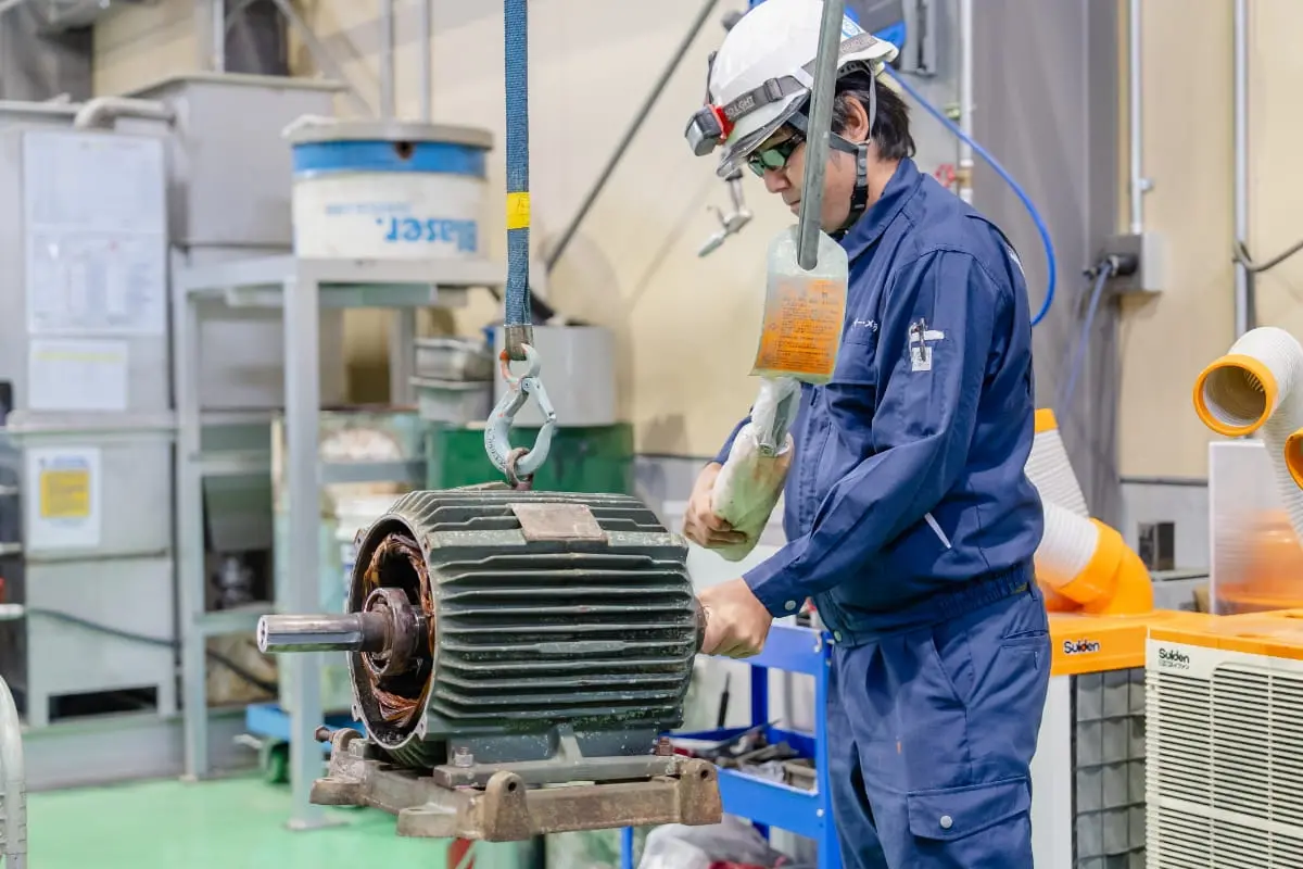 青空の下でプラント設備を見上げる作業員の姿