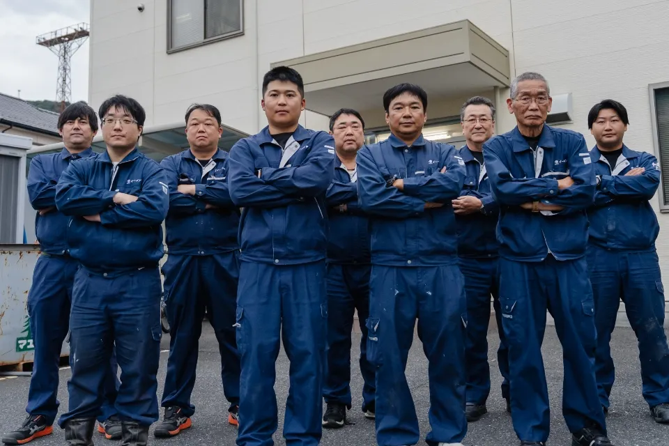 作業着を着た社員たちが屋外で並んで撮影した集合写真